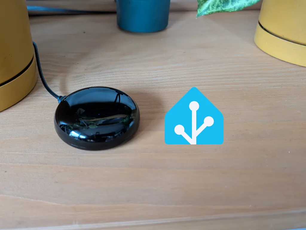 Małe, czarne i błyszczące urządzenie XIAO Smart IR Mate umieszczone na drewnianym blacie obok logotypu Home Assistant.